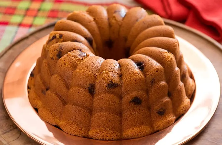 Bolo de fubá com pedaços de goiabada, feito em forma de bolo decorada, servido em um prato de cobre.
