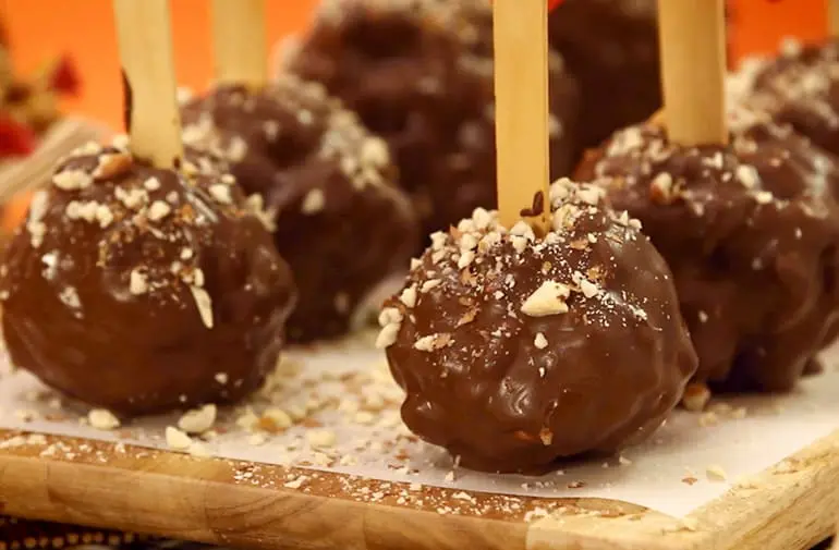 Maçã do amor feita de pipoca, coberta com chocolate e amendoim triturado, espetada em palitos