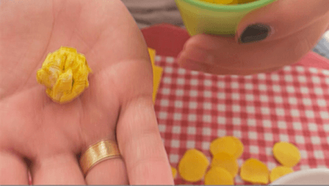 Uma mão segura bolinha de guardanapo amarelo amassado, com toalha xadrez ao fundo
