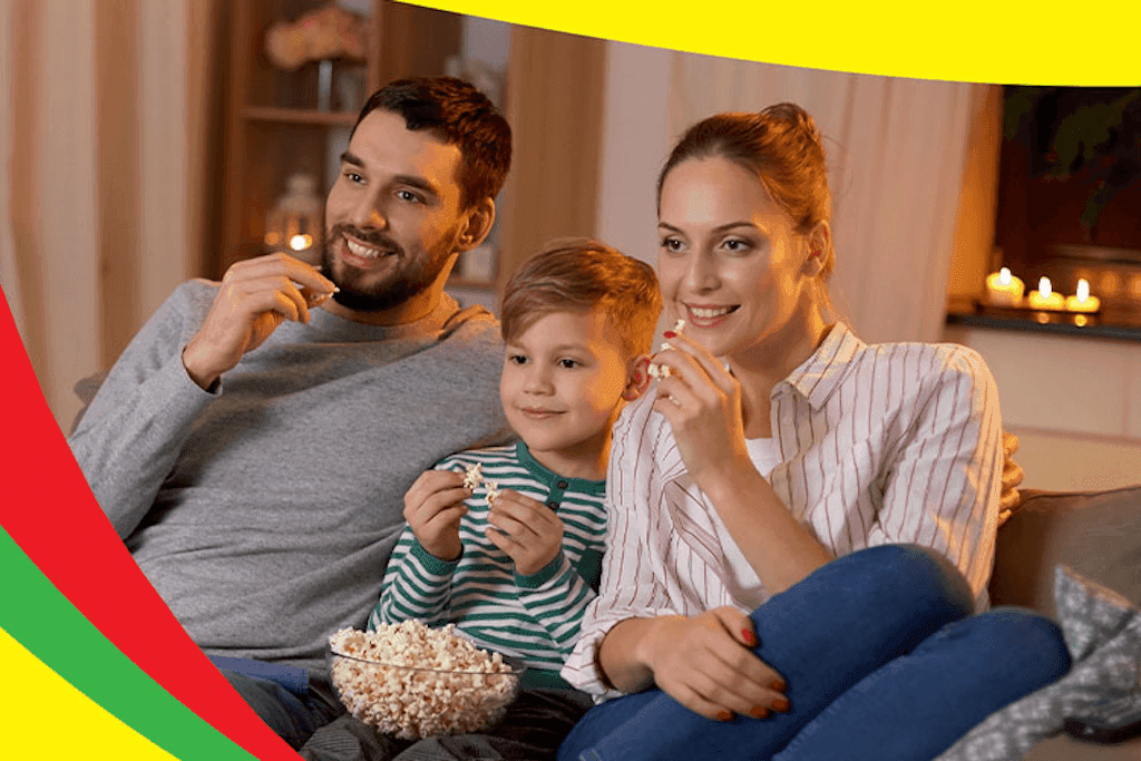 Casal de adultos e um menino comem pipoca salgada de um bowl de vidro enquanto assiste televisão