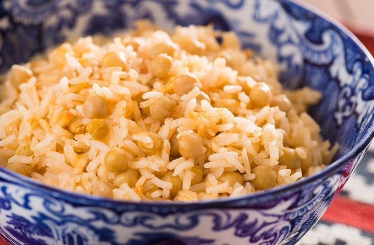 Arroz com grão de bico e molho de tomate, tom amarelado, em tigela de porcelana azul em estilo colonial