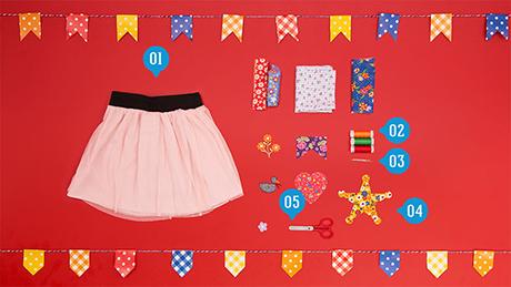Saia rosa ao lado de retalhos, fitas coloridas, linha e cola sobre fundo vermelho com tema de festa junina