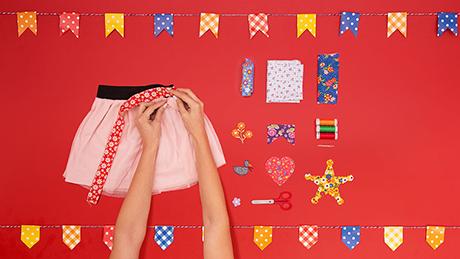 Uma pessoa costura retalho vermelho colorido como um cinto para saia rosa, ao lado de retalhos com tema de festa junina