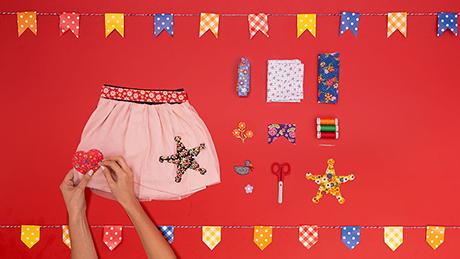 Mãos costuram saia de retalhos de coração e estrela de xerife, fazendo roupa customizada para festa junina