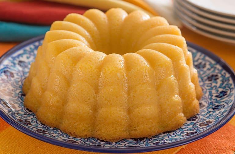Bolo de fubá cremoso e dourado, assado em forma ondulada, servido em prato de porcelana decorado