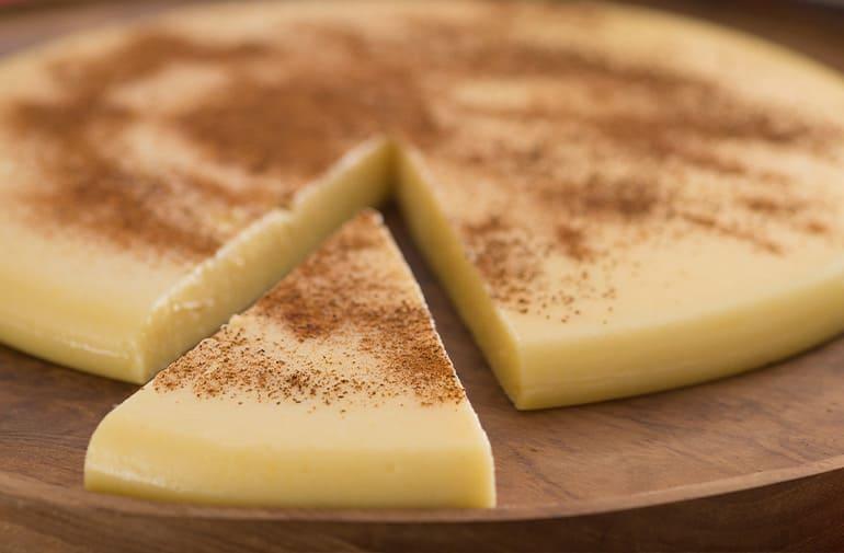 Canjiquinha de São João servida em prato de madeira, com fatia cremosa e finalizada com canela polvilhada