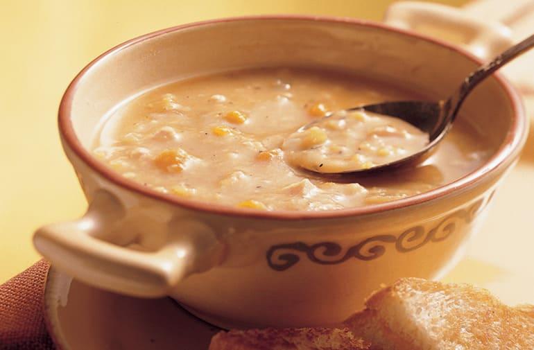 Pote de sopa artesanal com alça, com creme de grão de bico e uma colher, servido com pedacinhos de pão
