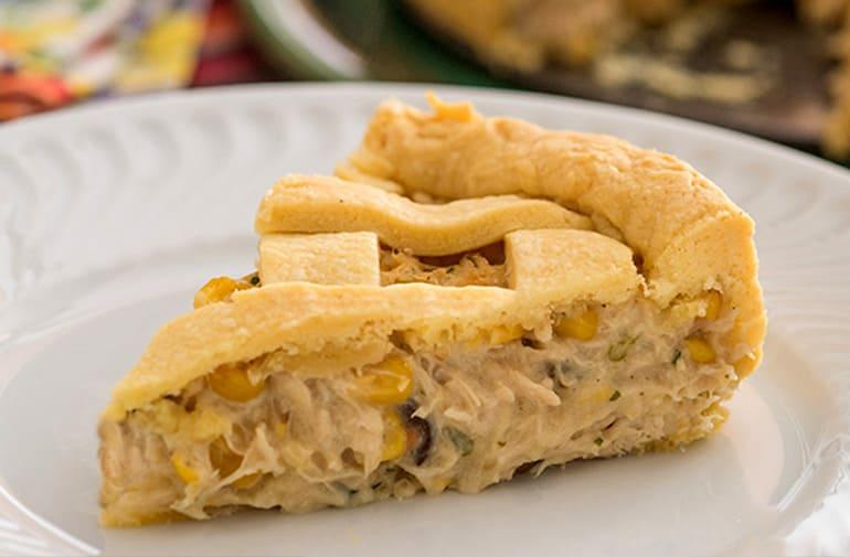 Pedaço de empadão recheado com creme de frango com pedacinhos de milho, servido em prato branco, receita de festa junina