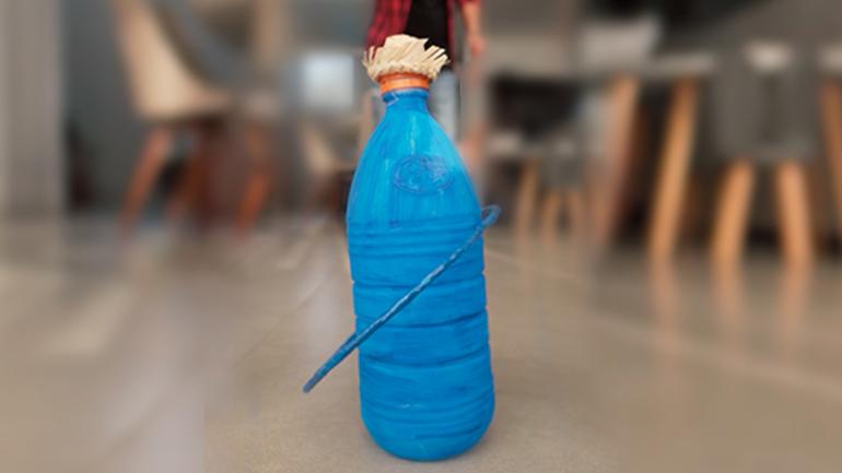 Garrafa pintada de azul com pequeno chapéu de palha de festa junina, com argola, em chão de sala de estar