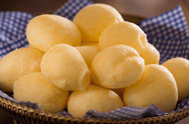 Porção de pão de queijo de tapioca e requeijão, servida em um cesto com guardanapo quadriculado