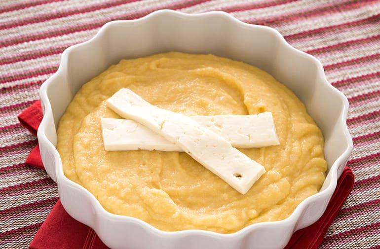 Polenta cremosa com queijo, coberta com duas fatias de queijo frescal, servida em travessa refratária