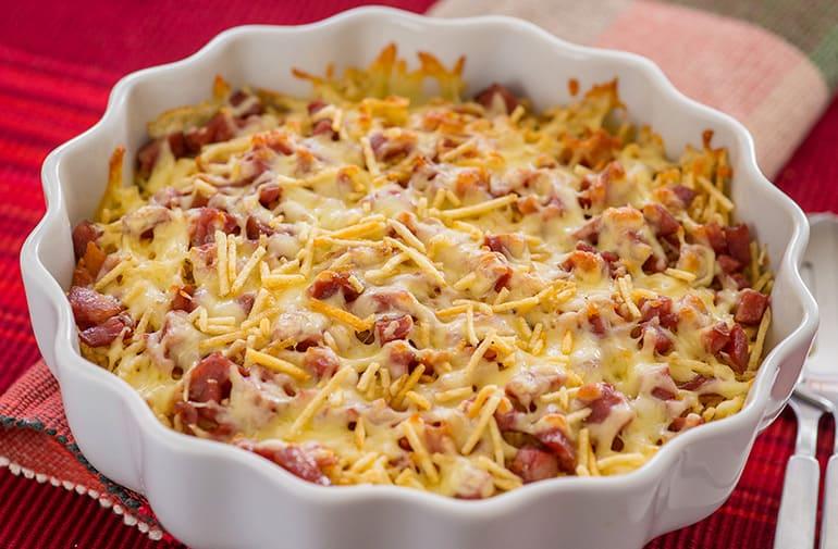 Pequena travessa ondulada de cerâmica branca com gratinado de batata palha, mussarela derretida, linguiça e bacon