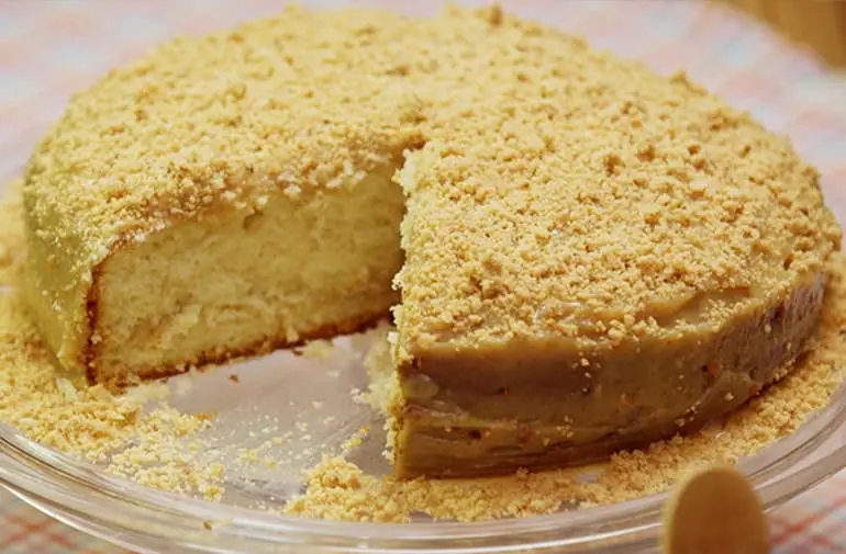 Bolo de paçoquinha feito com mistura pronta para bolo, servido em prato de vidro, com uma fatia retirada, massa fofinha