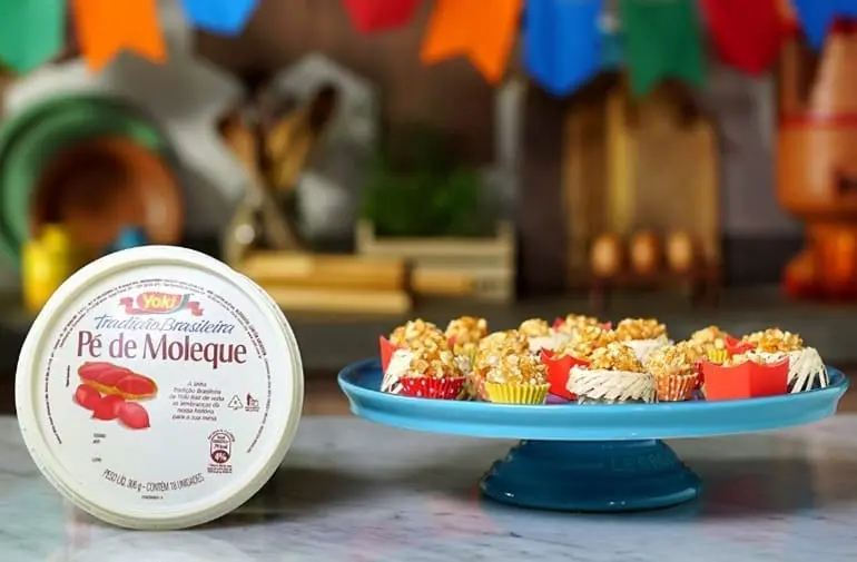 Brigadeiros de pé de moleque em forminhas coloridas, com embalagem Yoki ao lado em decoração de festa junina