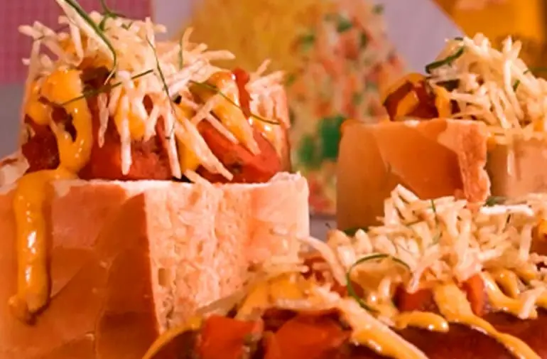Mesa decorada com cachorro-quente no pão com salsicha, maionese de batata palha, molho cremoso e ervas frescas