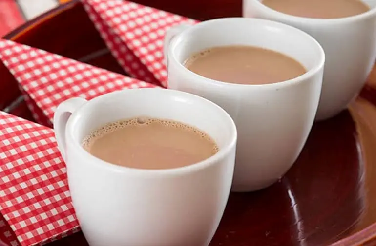Três xícaras de chocolate quente com canela servidos em uma bandeja com guardanapos quadriculados