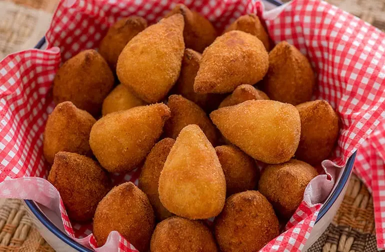 Porção grande de coxinha de purê de batata, servida em cesta de aperitivo com guardanapo quadriculado