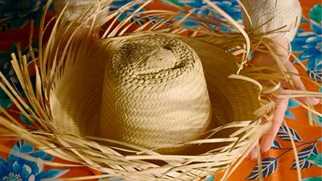 Uma pessoa segura um chapéu de palha típico de festa junina, com muitas pontas, sobre uma mesa de toalha florida