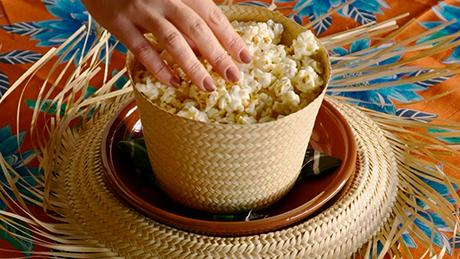 Um cesto com pipoca feito com a parte superior de um chapéu de palha, sobre um sousplas decorado com a aba do chapéu