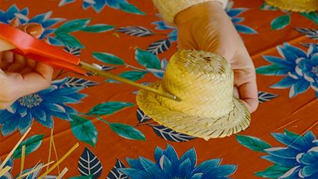 Uma pessoa recorta a aba de um mini chapéu de palha de festa junina para fazer decoração artesanal