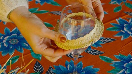 Decoração de mesa para festa junina, uma pessoa coloca uma pequena aba de chapéu de palha em uma taça de vinho