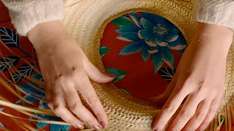 A aba do chapéu de palha com um furo no lugar do topo é posicionada sobre uma mesa com toalha floral