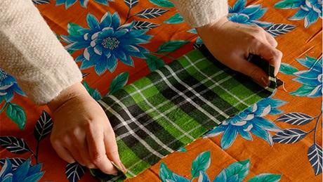 Uma pessoa decora uma mesa de festa junina segurando um retalho xadrez com quadriculados verdes