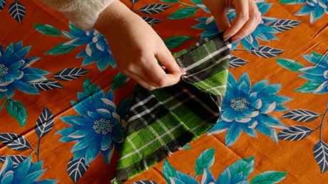 Um guardanapo xadrez com padrão verde é dobrado no formato de um losango, em preparação de mesa decorativa de festa junina