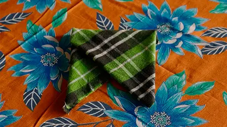 Lenço xadrez verde dobrado sobre toalha floral, para fazer um guardanapo decorativo de festa junina