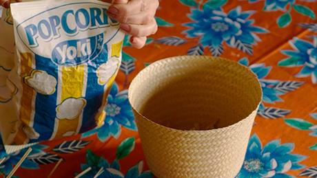 O topo de um chapéu de palha que teve a aba recortada serve como cesto para um pacote de pipoca de microondas Yoki