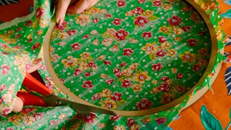 Pessoa recorta bordas de tecido de festa junina e encaixa entre dois bastidores de tecido, formando um quadro decorativo