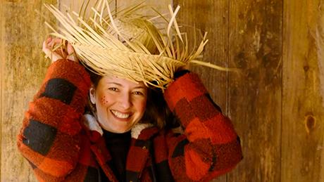 Mulher sorridente com camisa xadrez flanelada de cor vermelha e preta veste chapéu de palha típico de festa junina