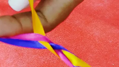 Detalhe de uma mão entrelaçando pequenas fitas coloridas e criando uma trança para decorar festa junina
