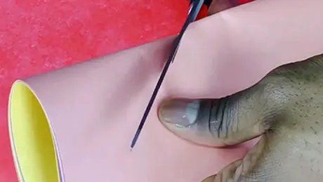 Com uma tesoura, mãos cortam um bandeirinhas de festa junina a partir de papel colorido dobrado