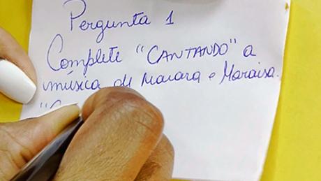 Uma pessoa escreve em bandeirinha de festa junina um desafio de cantar música de Maiara e Maraísa