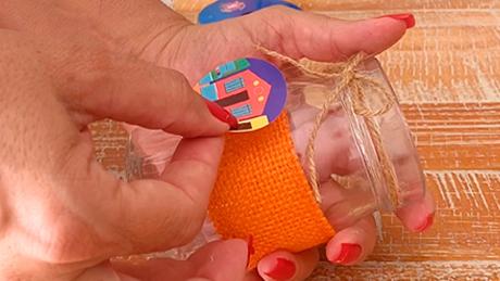 Mãos colam ilustrações típicas de festa juninha em potinhos artesanais de decoração de mesa para festa