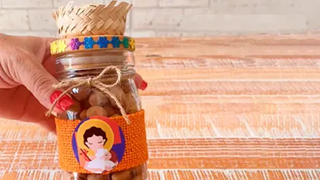 Mão segura potinho de vidro decorado e customizado para festa junina com amendoins Yoki dentro do recipiente