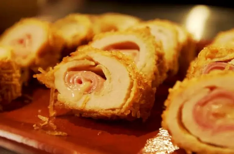 Enroladinhos de frango recheado com queijo e presunto, empanados com batata palha e cortados ao meio