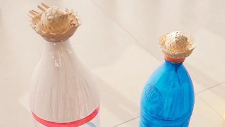 Duas garrafas estão lado a lado em atividade de festa junina, decoradas e customizadas, cada uma com um mini chapéu de palha