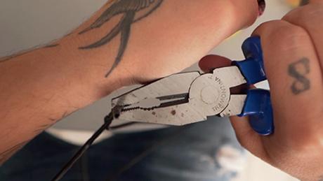 Mãos desfazem um cabide com a ajuda de um alicate, para formar uma argola que será utilizada em brincadeira de festa junina