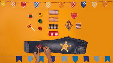 Mãos costuram retalhos em calça jeans, como remendo xadrez e estrela de xerife para traje de festa junina