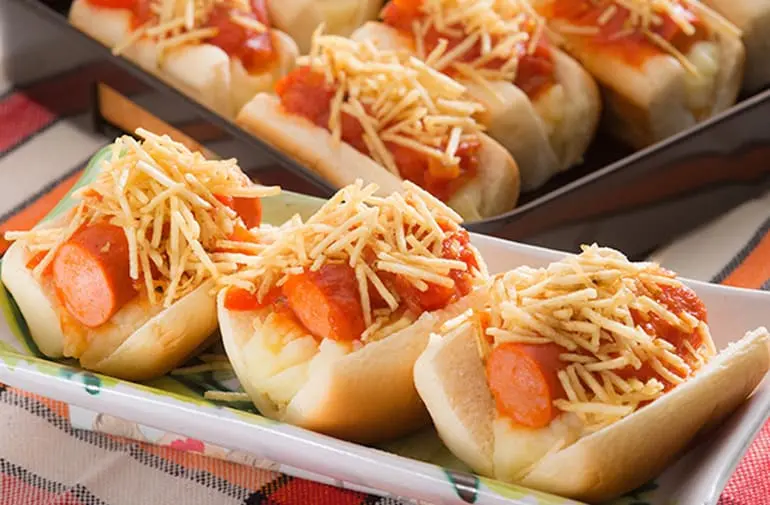 Porção de mini cachorros-quentes com purê, salsicha, molho de tomate e batata palha, servidos como lanchinho