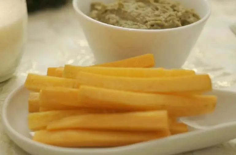 Palitos de cenoura servidos em um prato ao lado de recipiente com patê de lentilha cozida