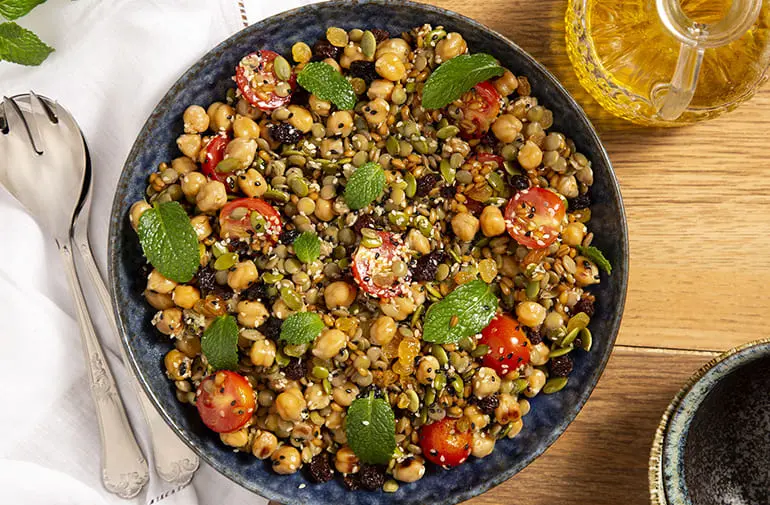 Salada de grãos e sementes com grão-de-bico, lentilha, tomate cereja e hortelã, servida em prato azul