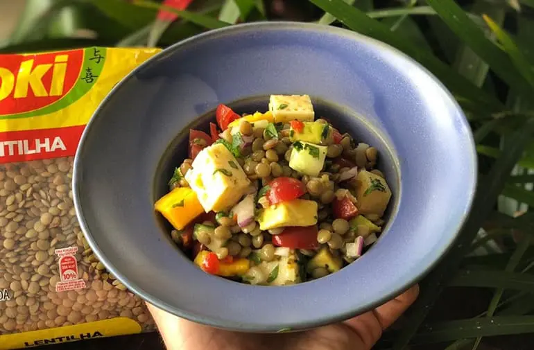 Salada de lentilha tropical com queijo minas, manga, tomate e pepino, em prato azul ao lado de pacote de lentilha Yoki.