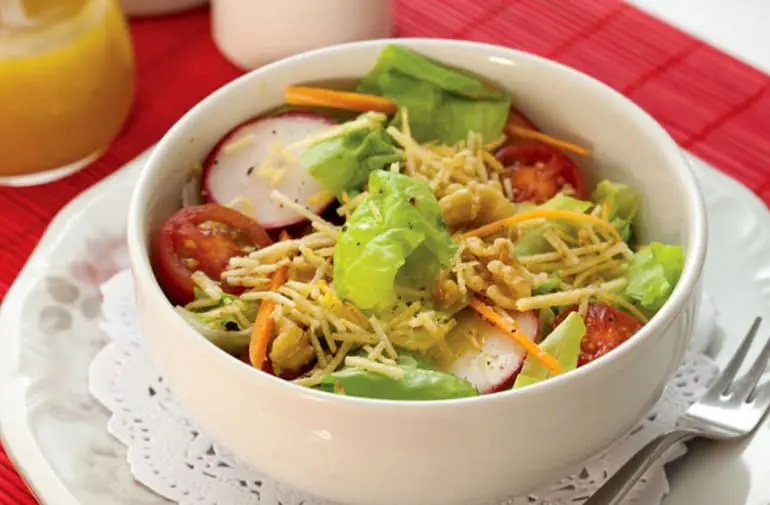 Salada Juliana fresca com batata palha, alface, tomate cereja, rabanetes, queijo ralado e nozes, servida em um bowl branco