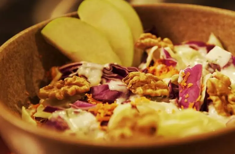 Salada de natal tropical com maçã, nozes, repolho e iogurte, servida em bowl de madeira