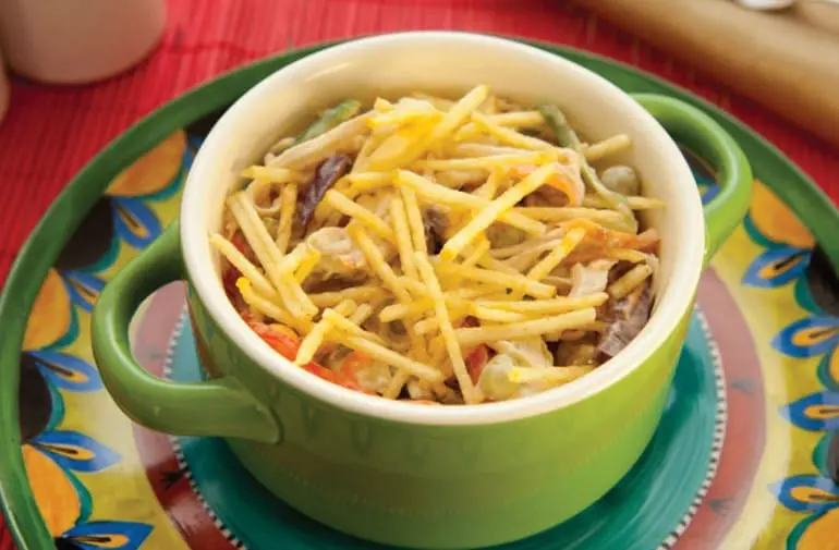 Tigela verde com salpicão de frango cremoso e grande variedade de ingredientes, coberto com batata palha