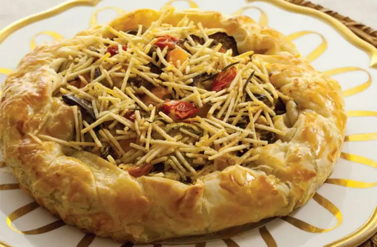 " Torta de massa folhada aberta, recheada com legumes como berinjela, abobrinha e pimentão, coberta com batata palha"